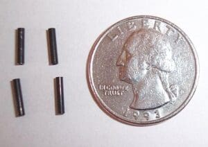 Four small black cylinders next to a quarter.
